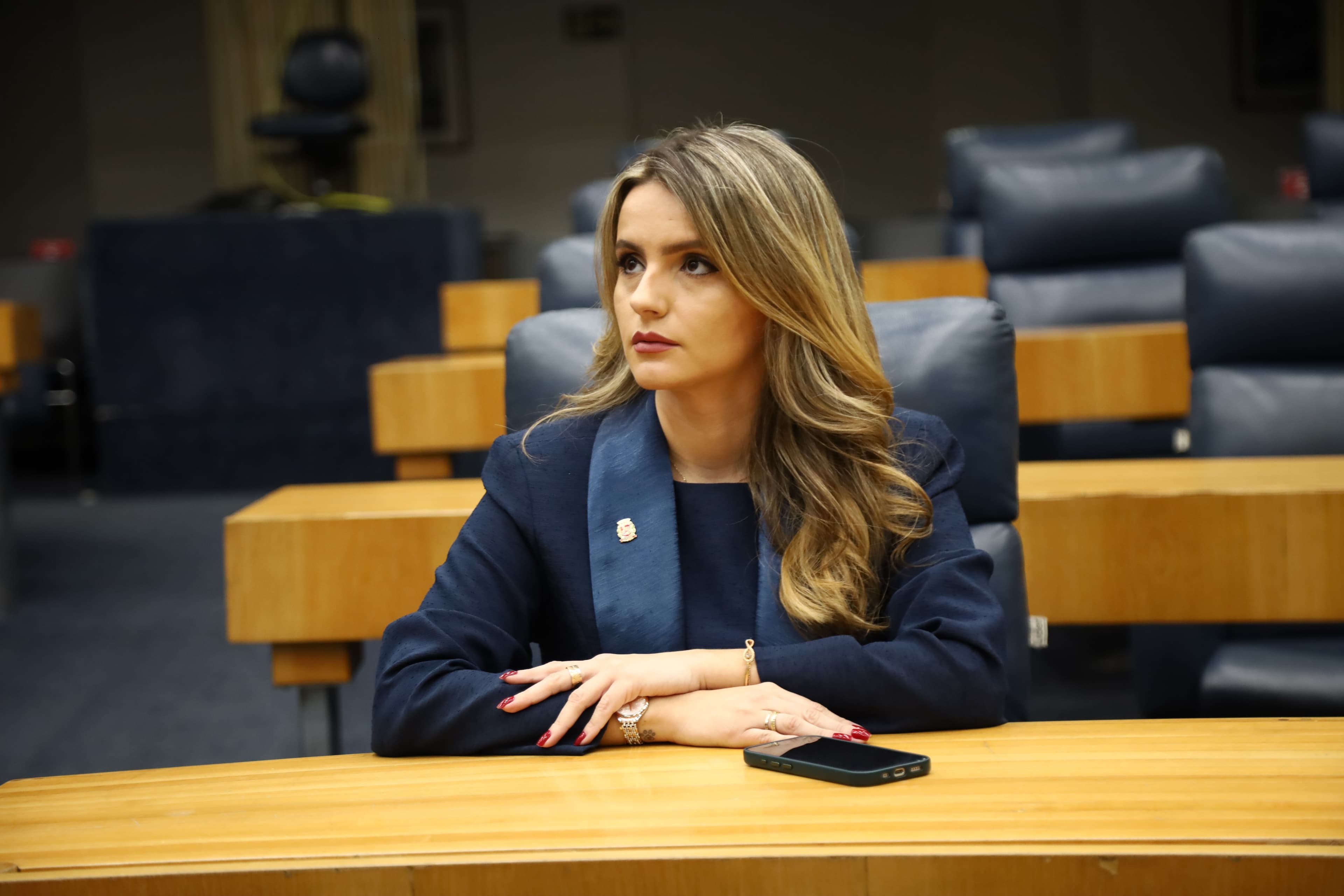 Amanda Vettorazzo, séria, sentada numa bancada do plenário da Câmara Municipal de São Paulo