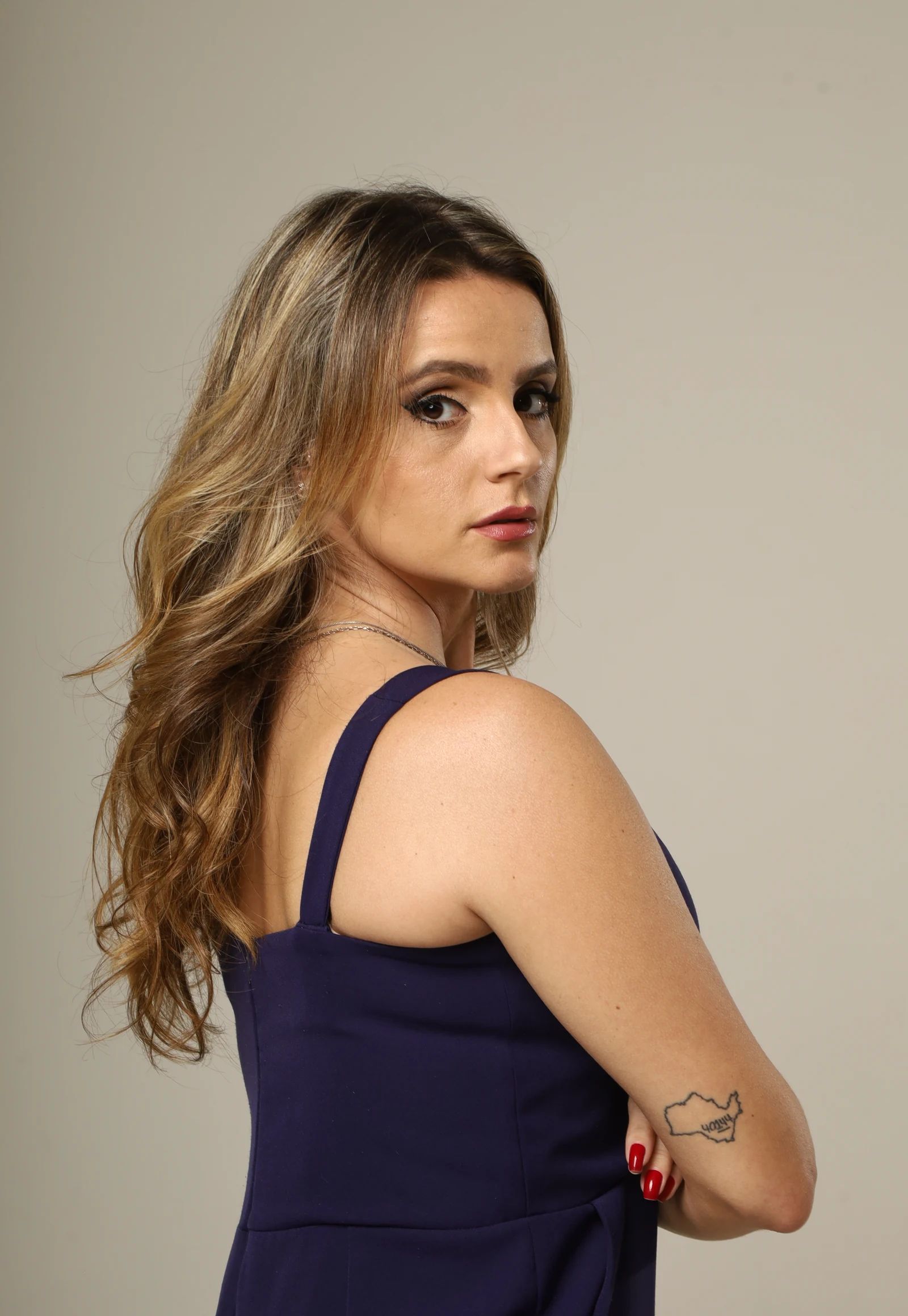 Retrato de Amanda Vettorazzo, de vestido azul-marinho e braços cruzados, olhando por cima do ombro